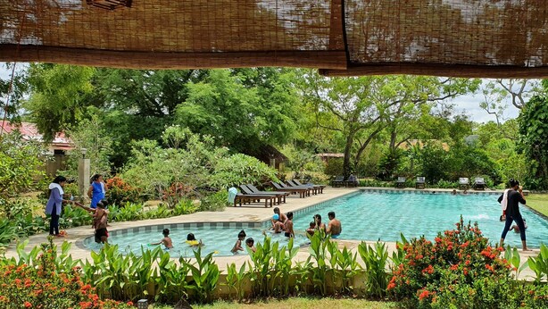 Piscina rodeada de vegetación exuberante y una zona de estar techada.