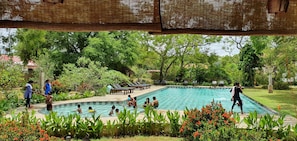 A swimming pool surrounded by lush greenery and a covered seating area. - Blue Turtle Hotel (Thissamaharama)
