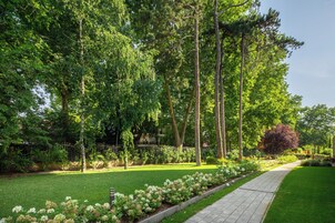 A well-maintained garden with a paved walkway, lush greenery, and flowering plants.