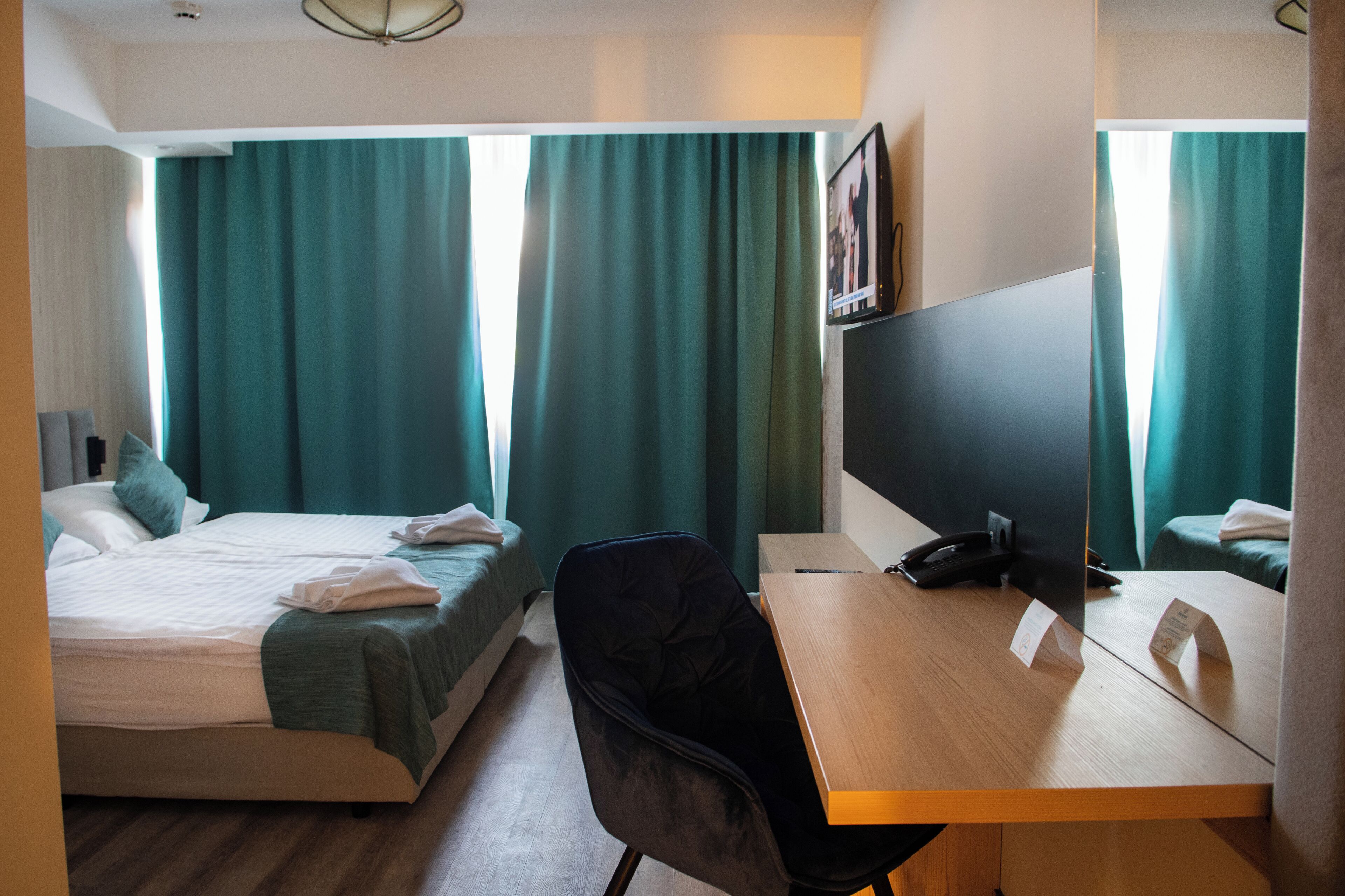 A hotel room with two beds, a desk, a chair, a desk lamp, and a large mirror.