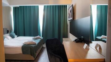 A hotel room with two beds, a desk, a chair, a desk lamp, and a large mirror.