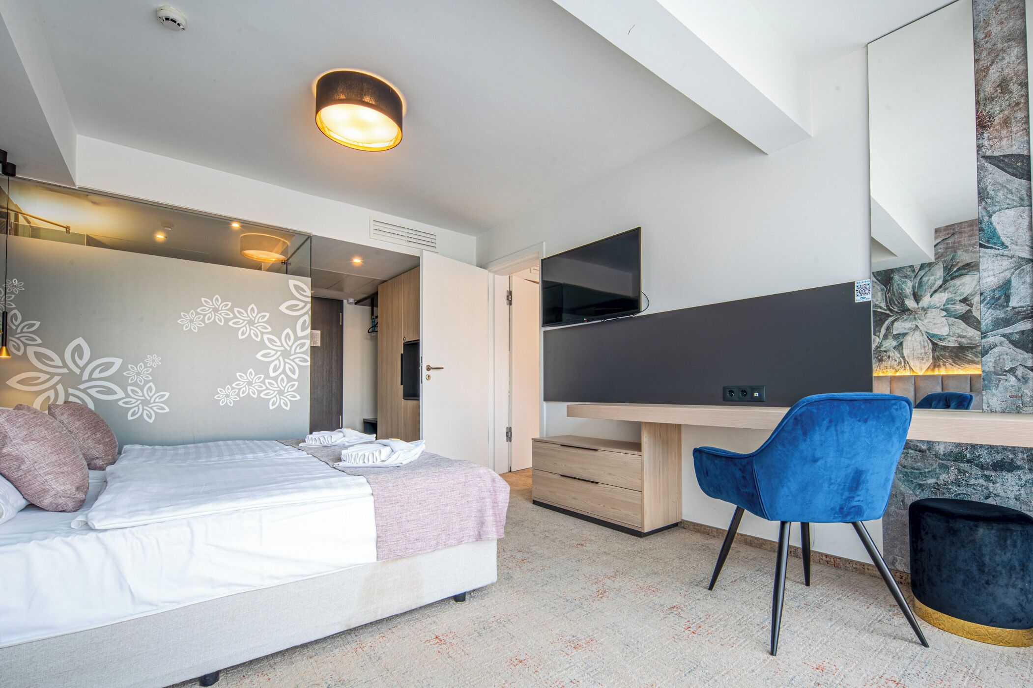A modern bedroom with a bed, a desk, a chair, and a TV.