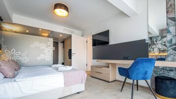 A modern bedroom with a bed, a desk, a chair, and a TV.