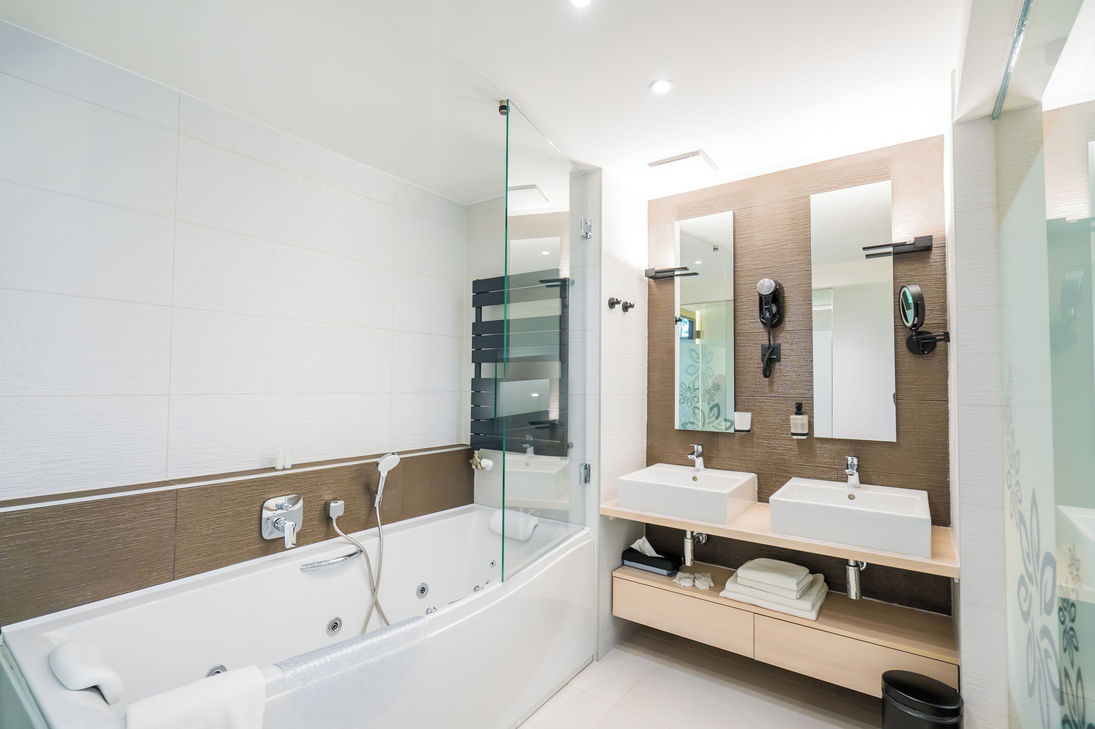 Un baño moderno con ducha de vidrio, dos lavamanos y tocador con espejo.