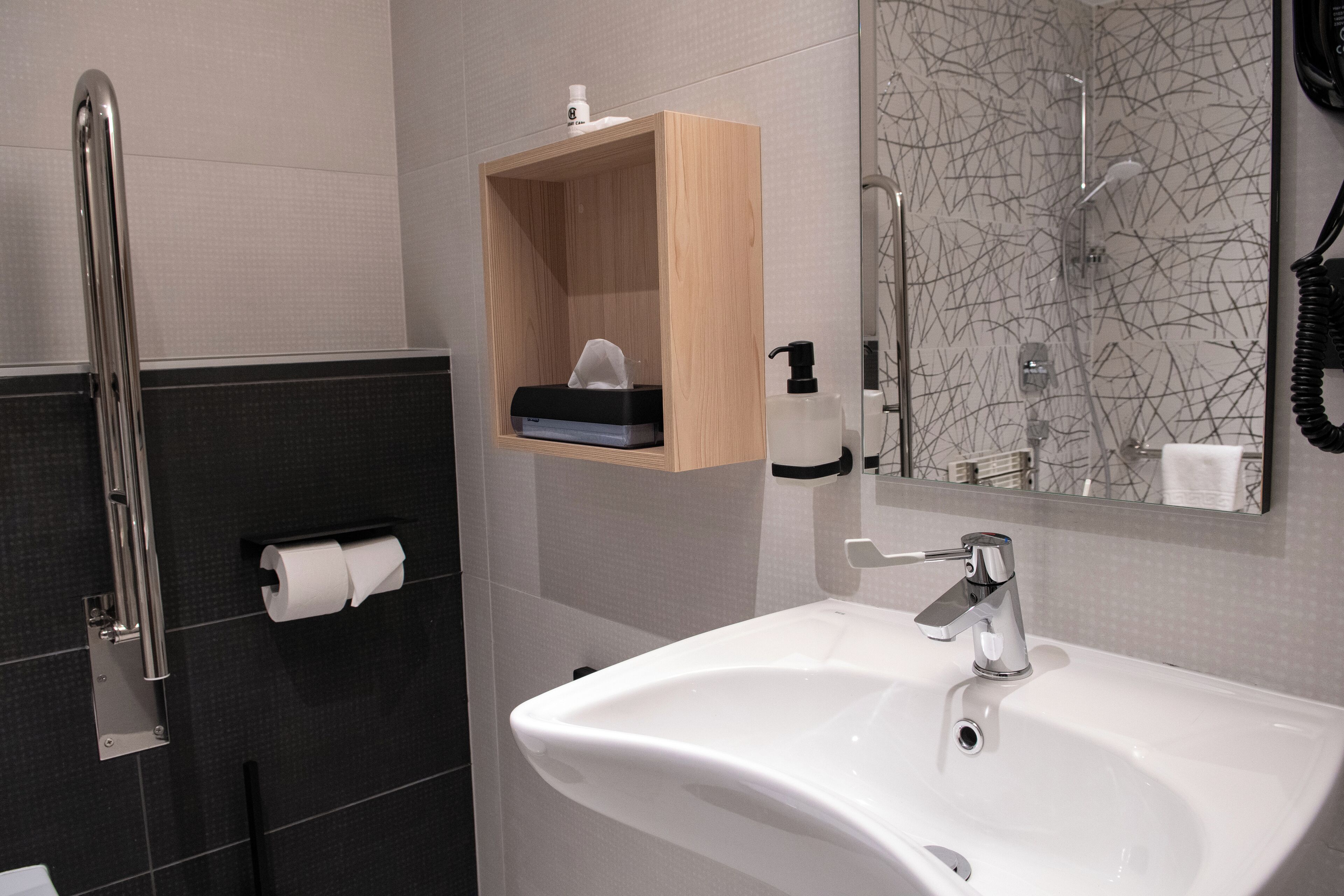 A modern bathroom with a white sink, a wooden medicine cabinet, a handrail, and a toilet paper holder.