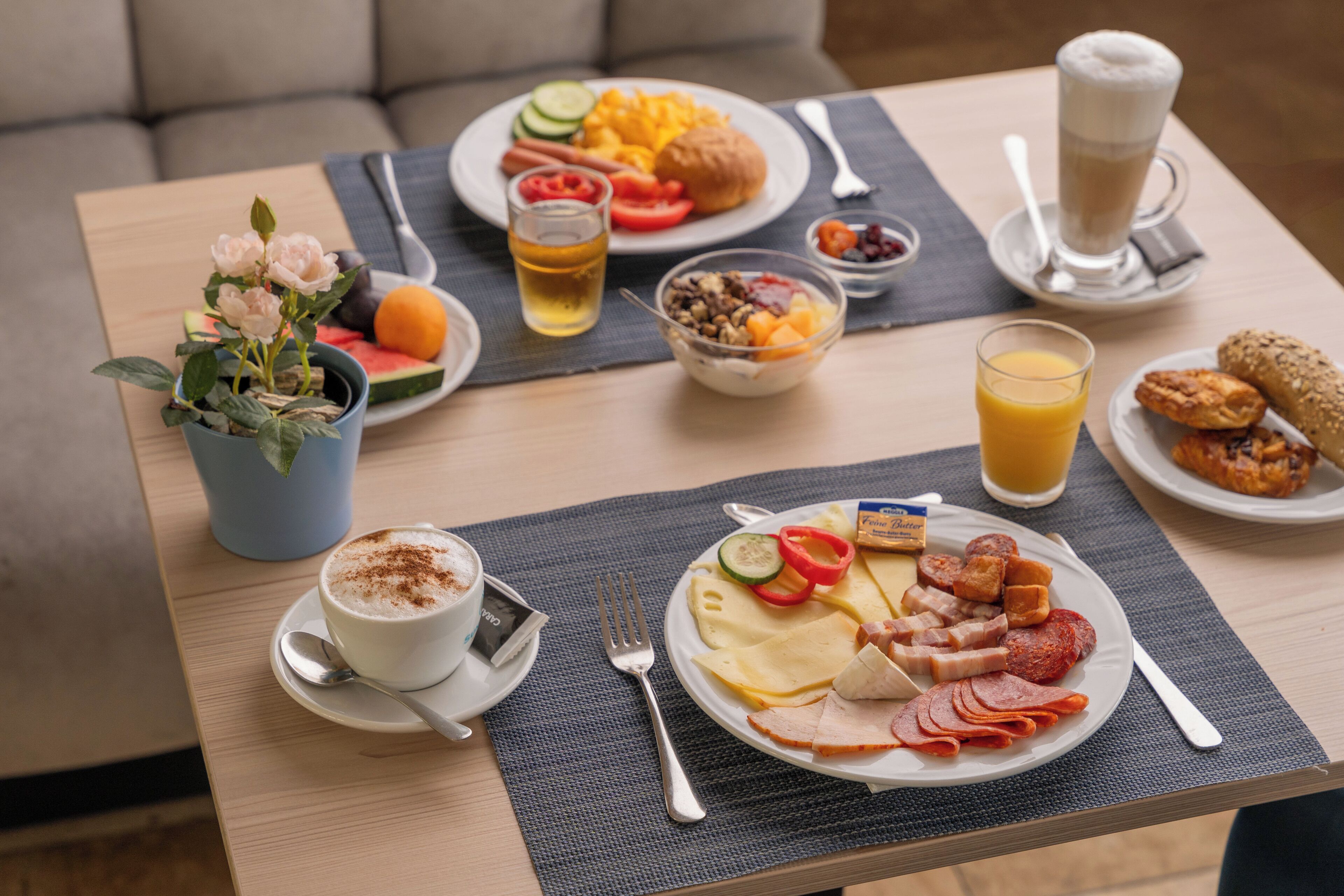 Una mesa de desayuno con diversas opciones de comida, una taza de café y un vaso de jugo de naranja.