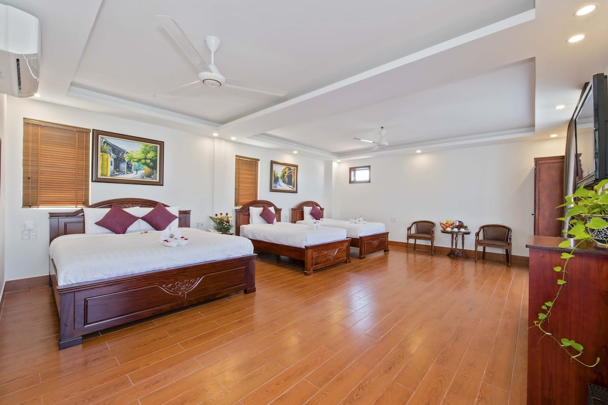 Une chambre d’hôtel avec trois lits en bois, un bureau, des chaises et un ventilateur de plafond.
