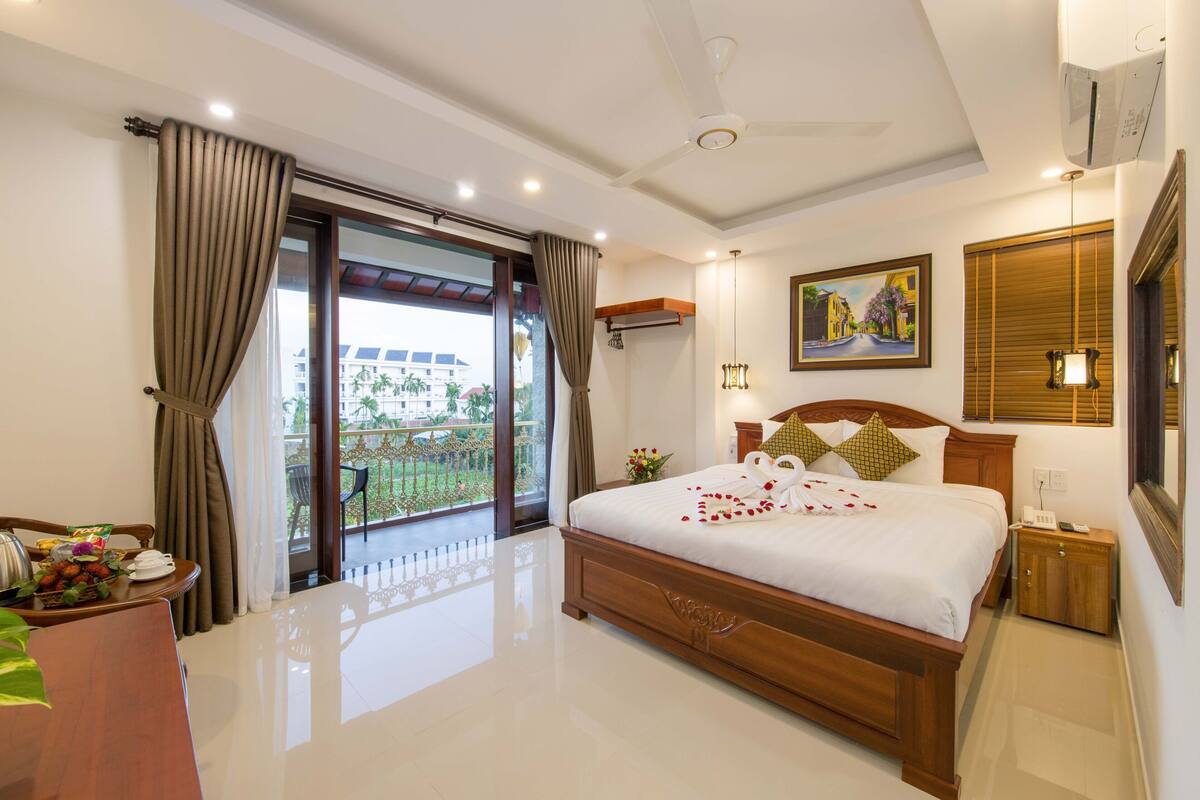 Une chambre d’hôtel avec un grand lit, un balcon avec vue, un coin repas et un tableau au mur.