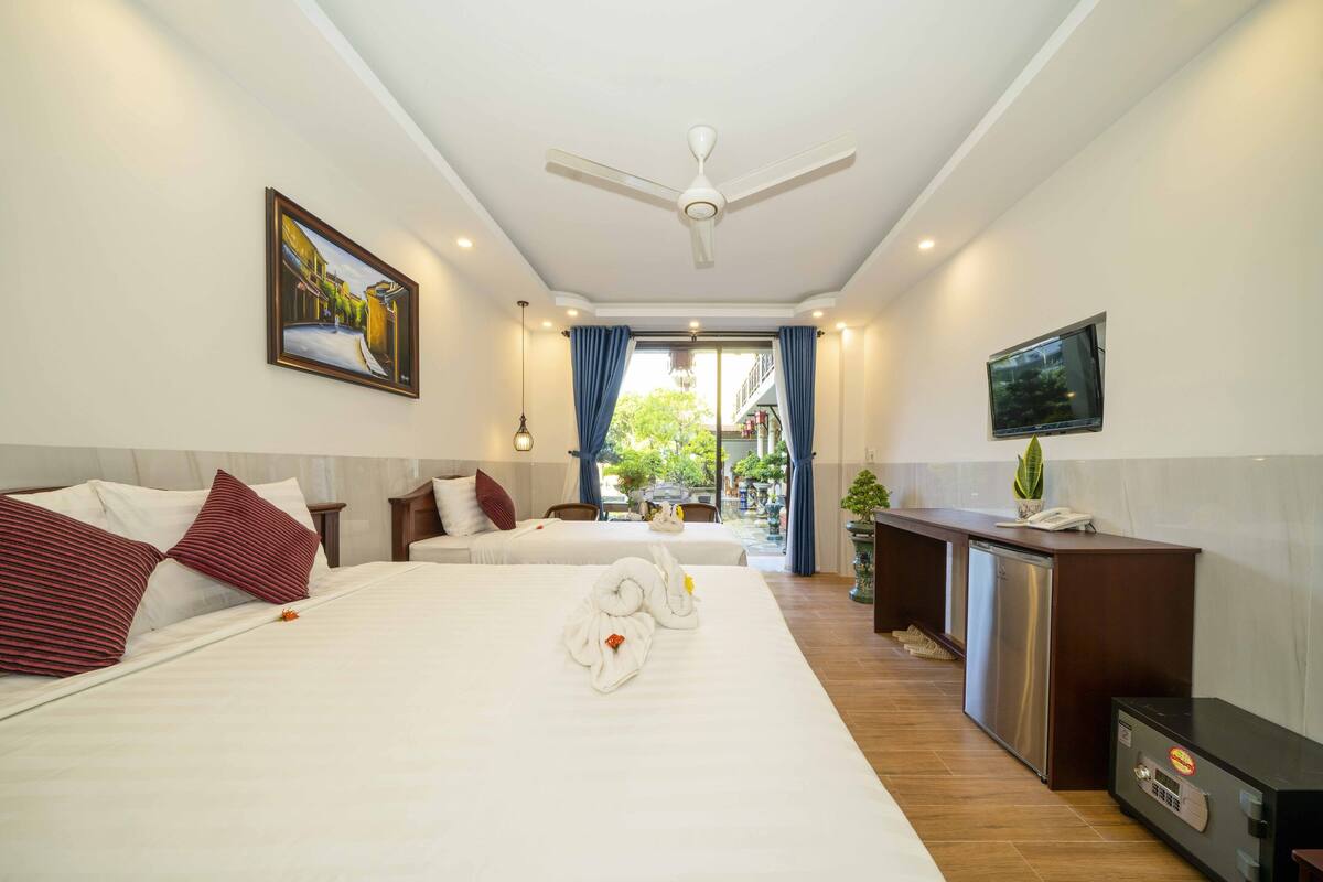 Une chambre d’hôtel avec deux lits, un ventilateur de plafond, une télévision, un minibar et une vue sur l’espace extérieur.