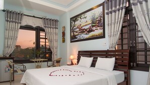Un dormitorio con cama, una ventana con cortinas, una mesa con sillas y un cuadro en la pared.