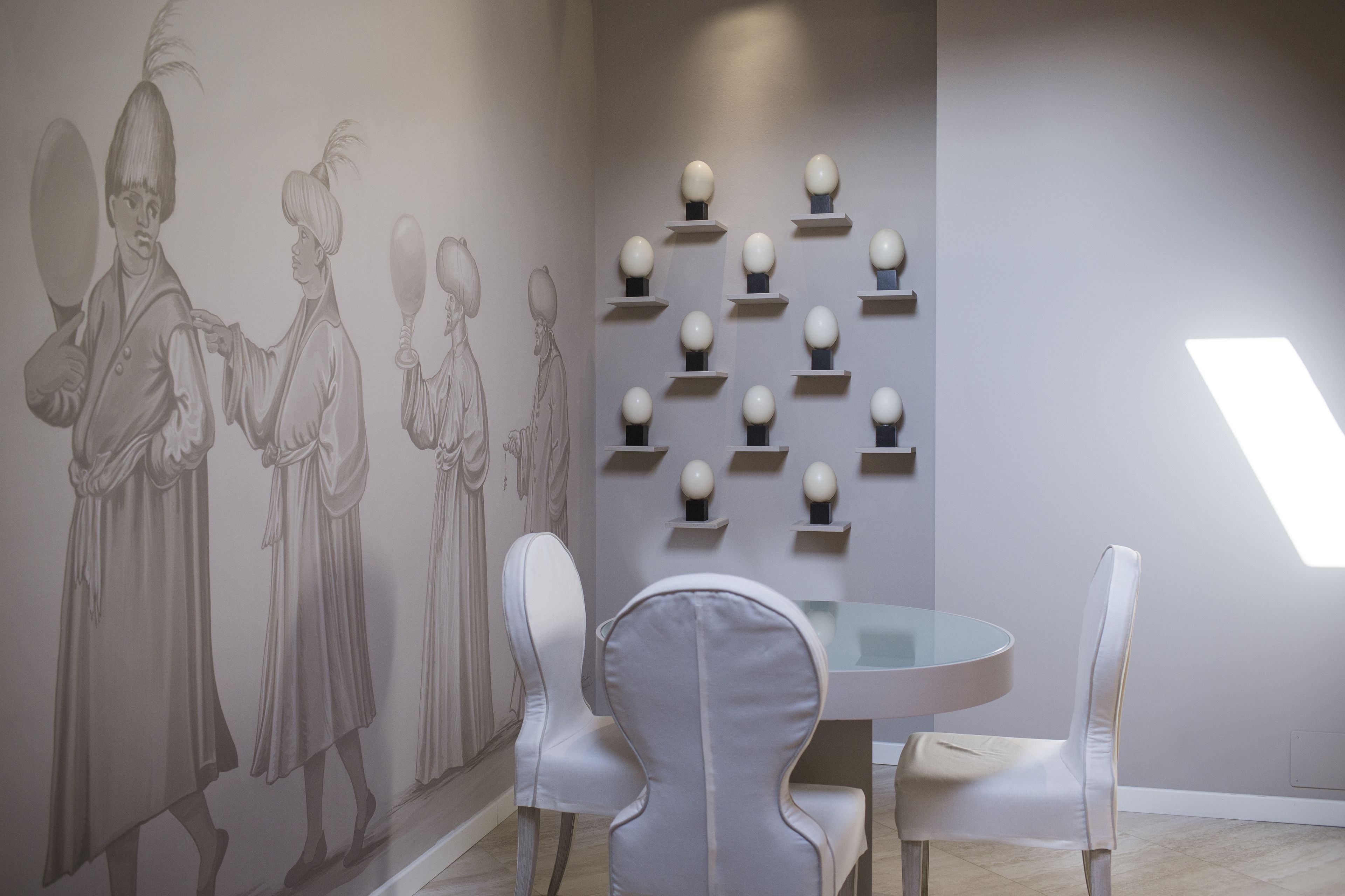 Un comedor con una mesa redonda, sillas blancas y una pared decorada con un mural.