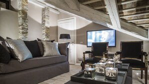 Un salon avec un canapé gris, deux fauteuils, une table basse avec des bougies, un téléviseur et un mur en pierre.