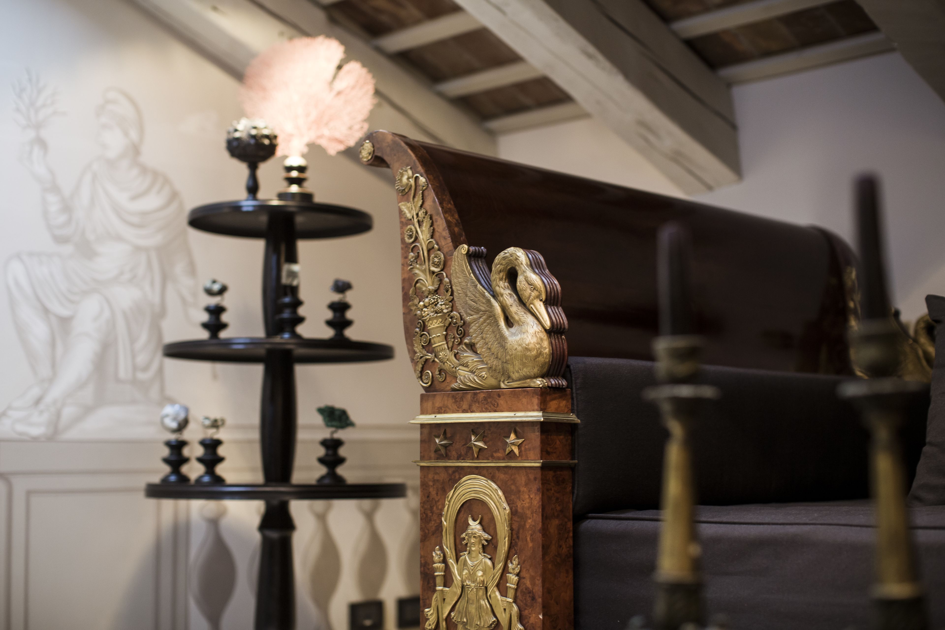 Una habitación con un sofá de color oscuro, un columnilla de madera decorativa con diseño de cisne, y una mesa negra con una vela encendida.