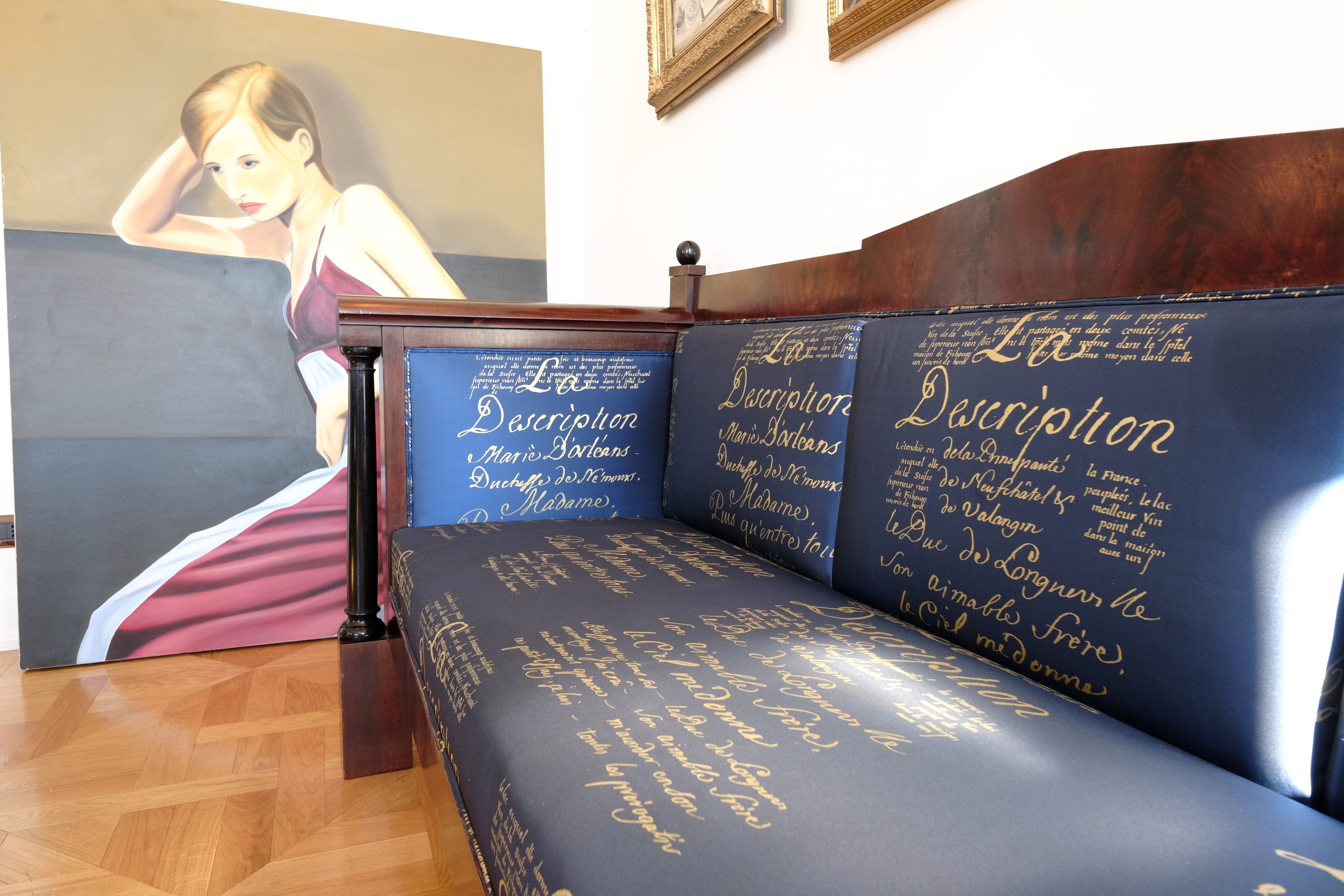 A room with a wooden bench and a large painting of a woman in a dress.