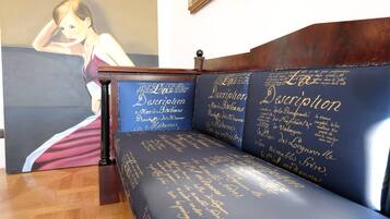 A room with a wooden bench and a large painting of a woman in a dress.