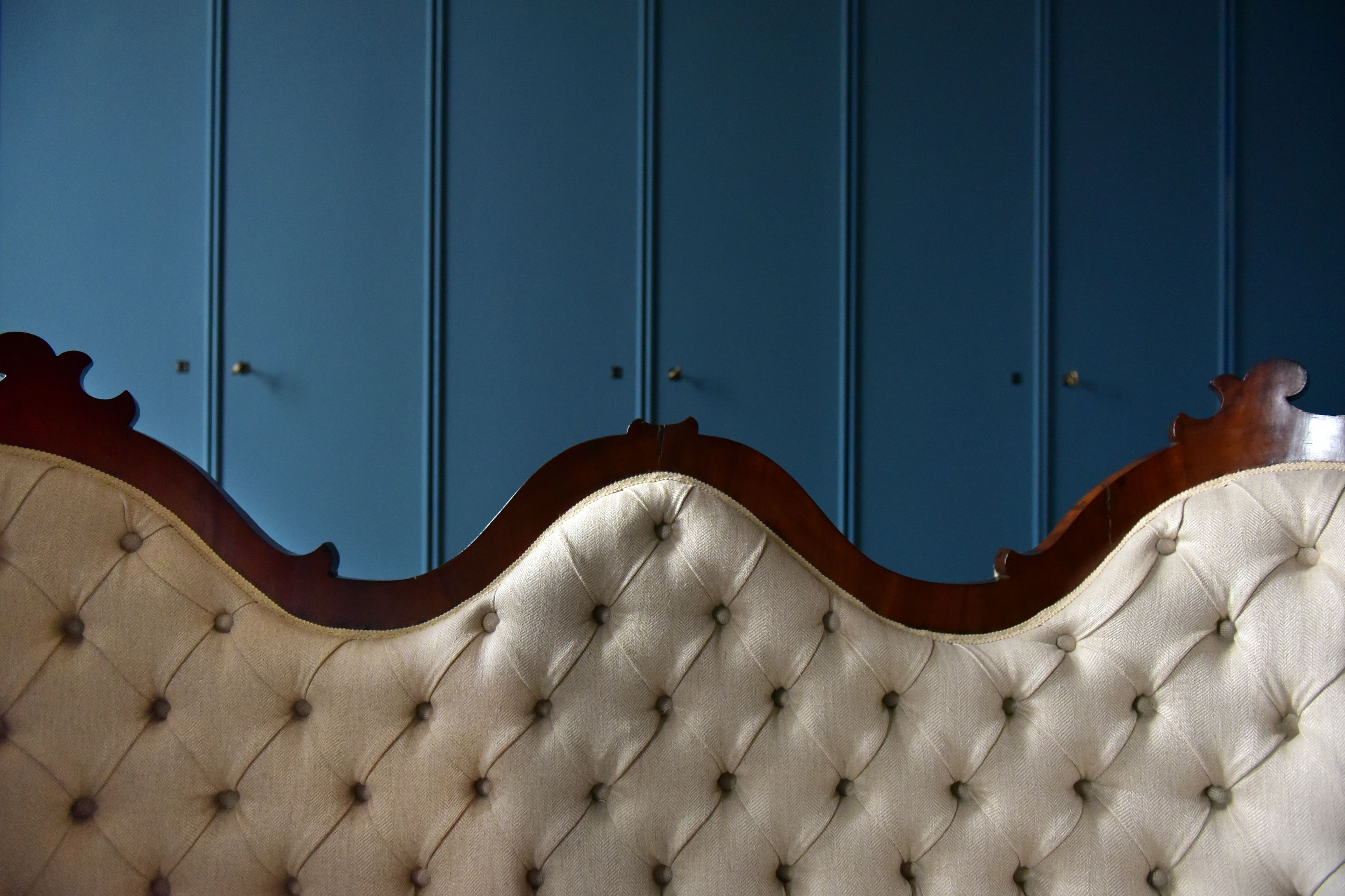 Een gestoffeerd hoofdbord met een gebogen ontwerp tegen een blauwe muur.