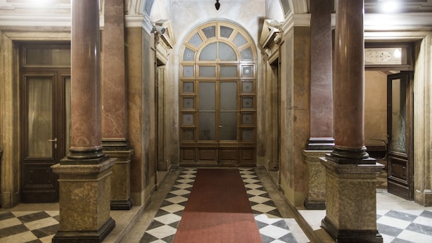 Un couloir doté d’un sol à carreaux, de grandes colonnes et d ’une imposante porte en arc de cercle.