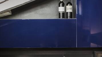 Une cuisine équipée d’un évier, d’une bouilloire et de deux bouteilles de vin, posées sur une étagère bleue.