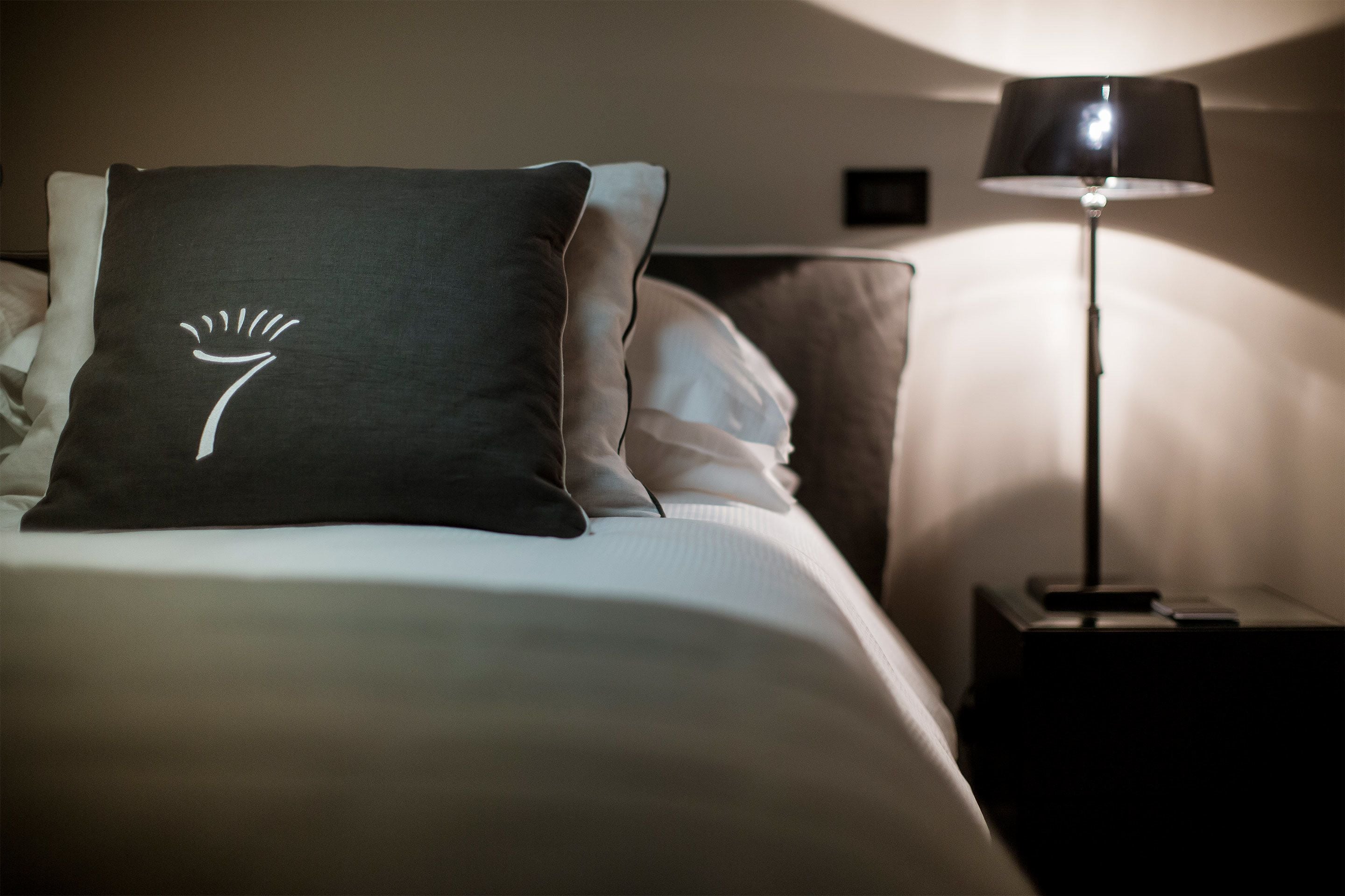 Un lit bien fait, avec un oreiller orné d’un motif blanc, une lampe de chevet et une horloge fixée au mur.