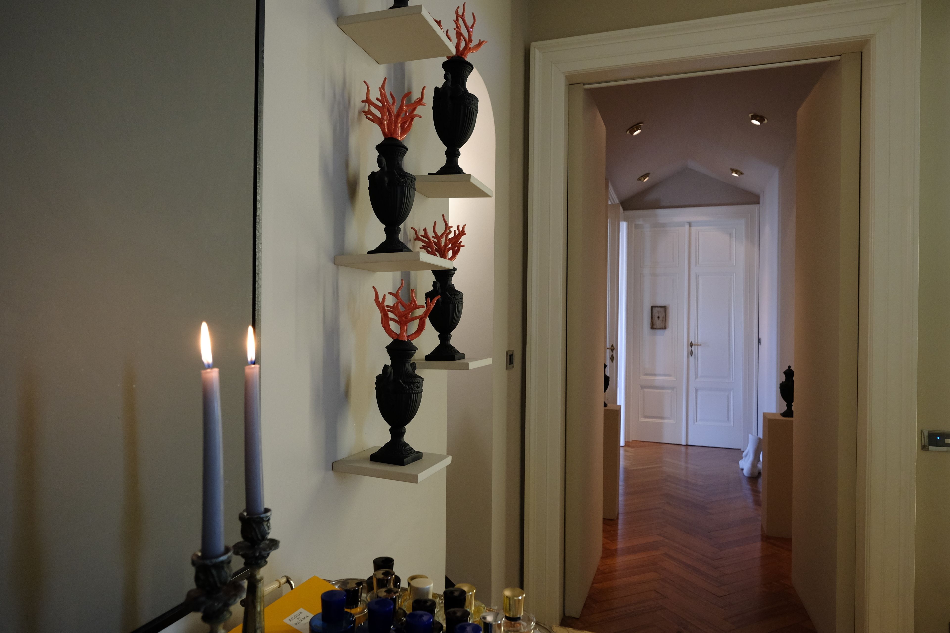 A hallway with a white door at the end, a shelf with decorative vases, and a candelabra with lit candles.