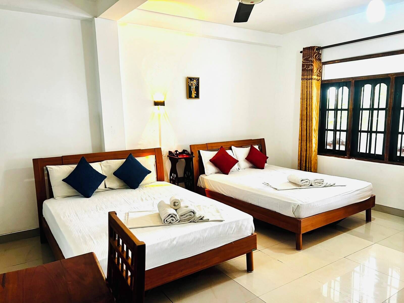 A hotel room with two wooden beds, white linens, and a small table with a lamp.