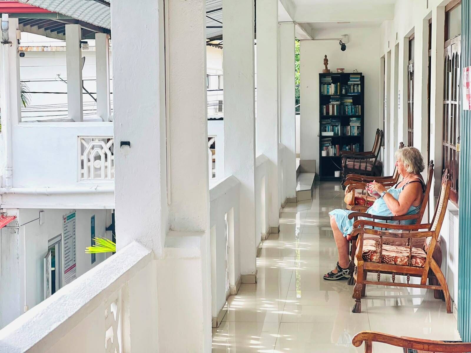 A covered balcony with a white railing, a wooden bench, and a bookshelf filled with books.