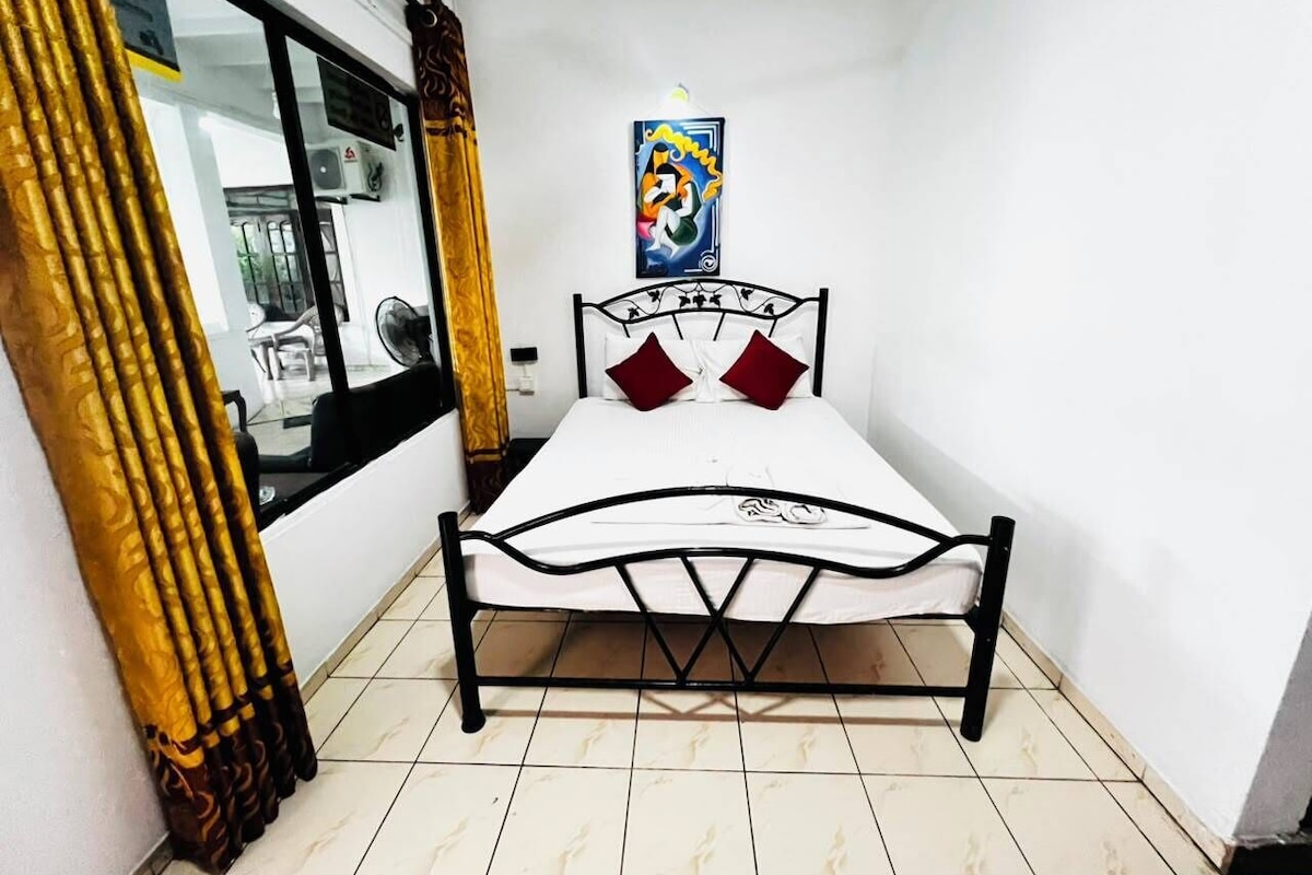 A small room with a bed, a window, and a wall-mounted picture.