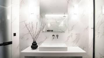 Un baño moderno con lavamanos de mármol blanco, un espejo y un jarrón negro con ramas.