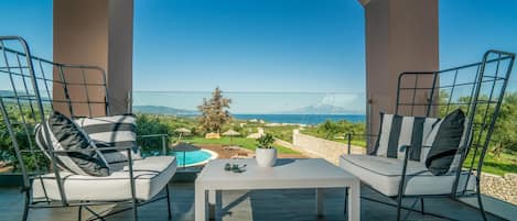 An outdoor seating area with two chairs and a table, overlooking a pool and a scenic landscape.
