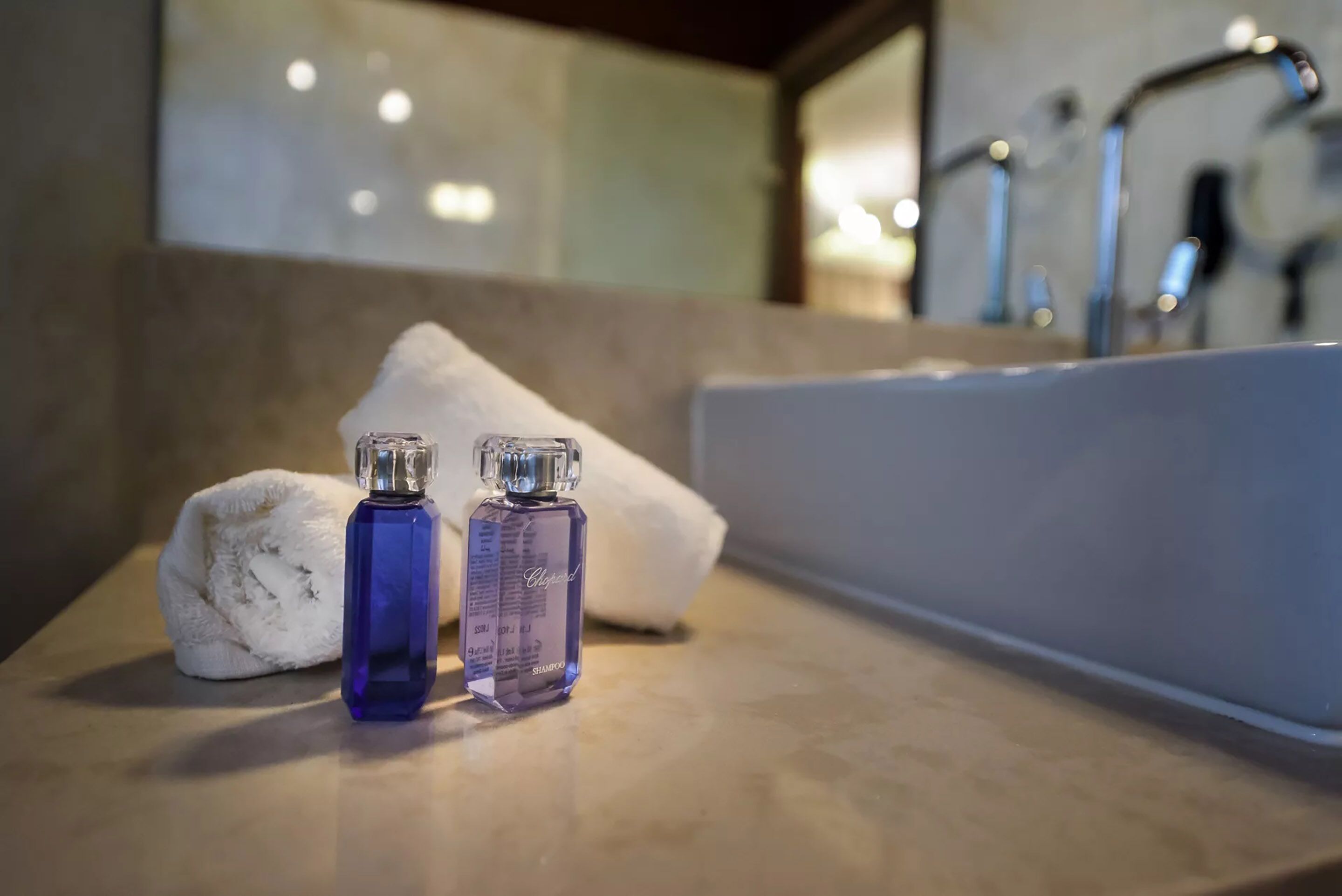 A bathroom with a bathtub, two bottles of shampoo, and a towel on a marble countertop.