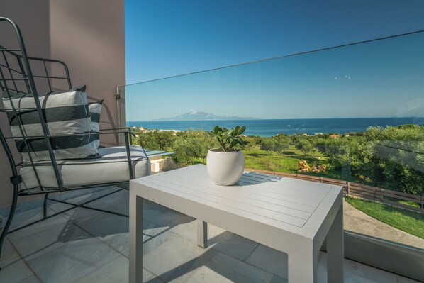 A balcony with a white table, a metal chair with cushions, and a potted plant. - Elegance Luxury Executive Suites - Adults Only (Zakynthos)