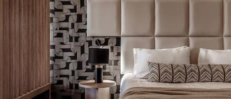 A bedroom with a tufted headboard, a round wooden nightstand, a black lamp, and patterned bedding.