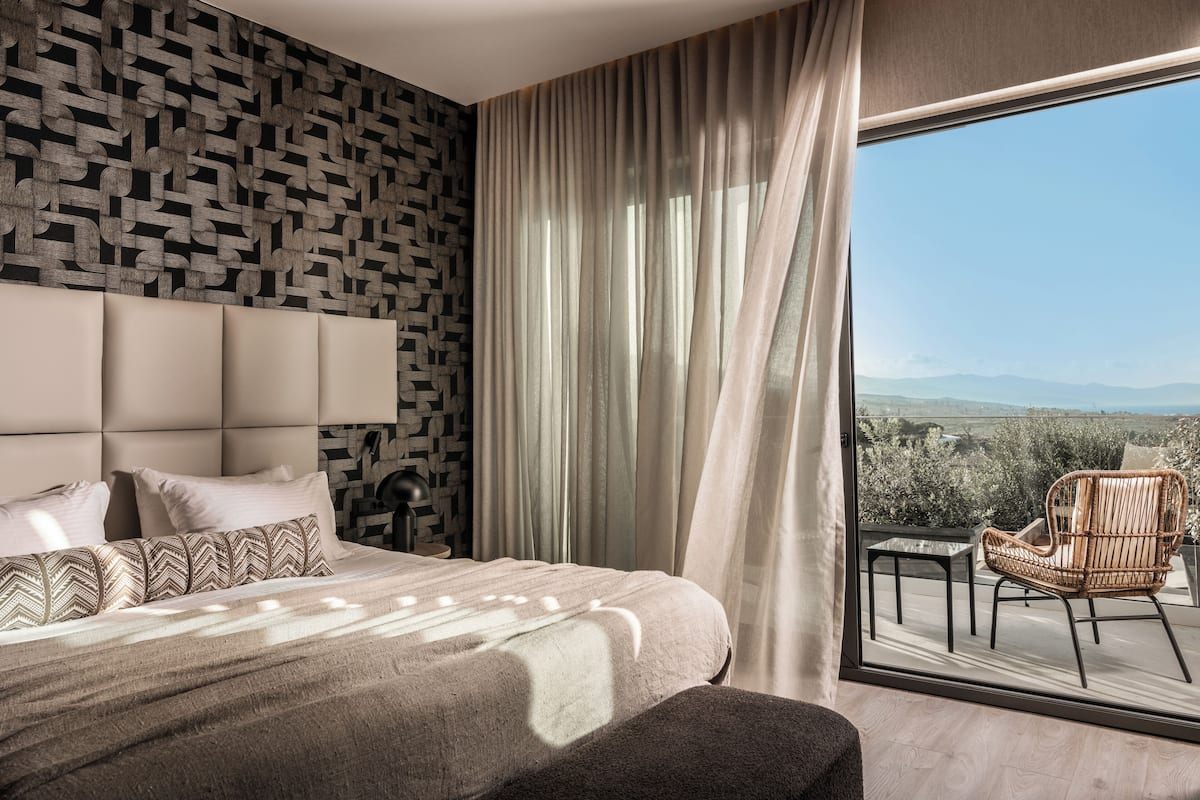 A modern bedroom with a large bed, a patterned wall, and a view of the outdoors through a large window.