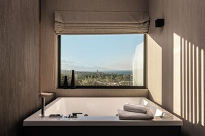 A modern bathroom with a large window, a bathtub, and a vanity with a mirror.