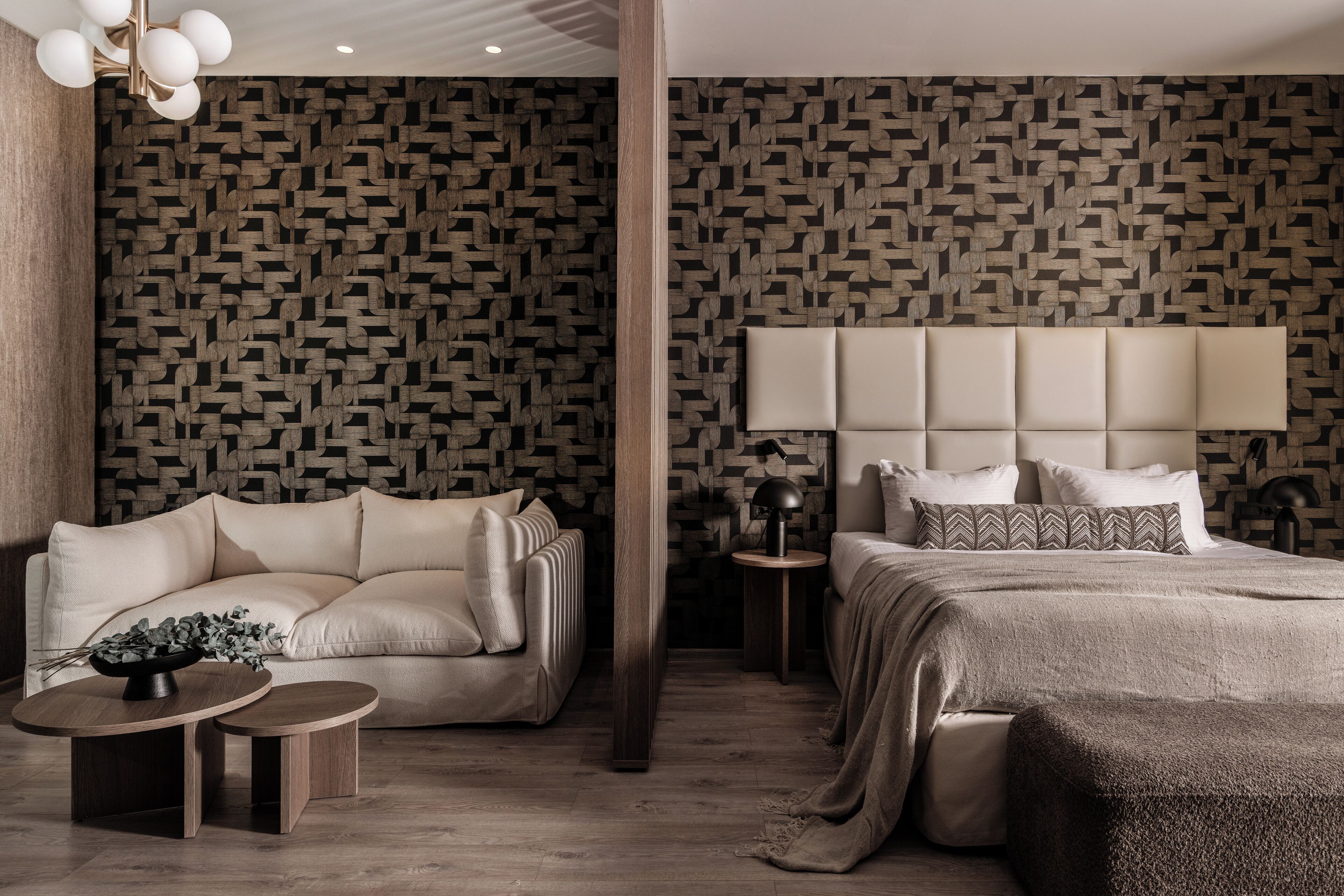 Une chambre à coucher moderne avec un papier peint à motifs, un grand lit avec une tête de lit, un canapé, une petite table sur laquelle est posé un vase de fleurs et une lampe.