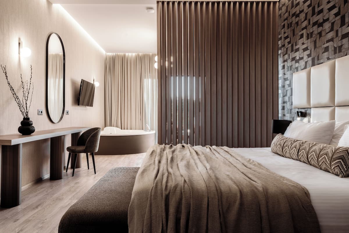 A modern hotel room with a bed, a desk, a chair, a television, and a large window with curtains.