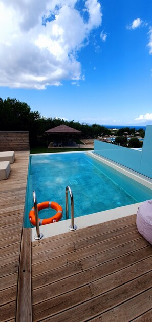 Une piscine avec une terrasse en bois, une bouée de sauvetage et un kiosque en arrière-plan.