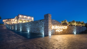Un muro de piedra con un letrero de neón que dice "Elegance" y un edificio con ventanas arqueadas al fondo.