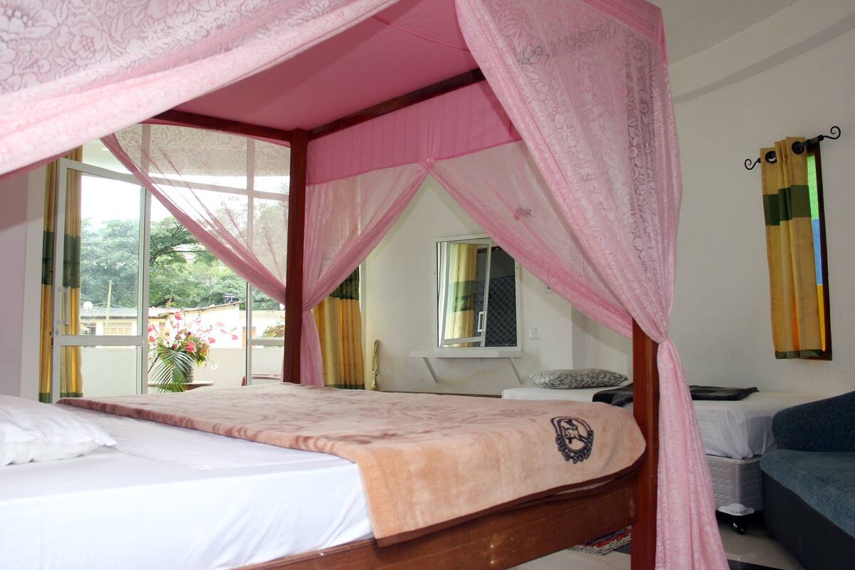 Een slaapkamer met een hemelbed, een klein tafeltje, een bank en een raam met gordijnen.
