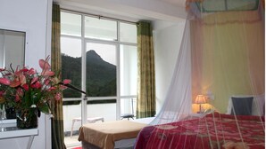 A hotel room with a bed, a desk with a vase of flowers, a chair, and a large window offering a mountain view. - White House Adam's Peak (Nallathanniya)