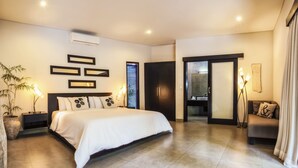 A modern bedroom with a large bed, bedside tables, a nightstand, a potted plant, and a bathroom visible through an open door. - Villa Lamunan (Legian)