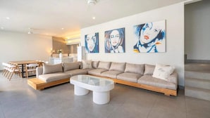 A modern living room with a sectional sofa, a glass coffee table, and a dining area with a wooden table and chairs. - Villa Lamunan (Legian)