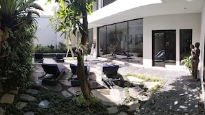 A modern outdoor patio with lounge chairs, a small table, and a sculpture. - Villa Lamunan (Legian)