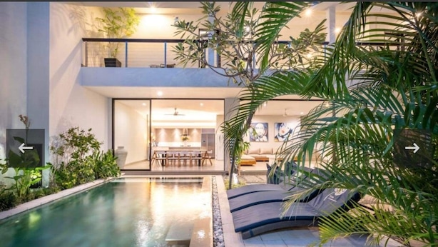 A modern house with a swimming pool, a dining area, and a living room with a sofa and a chair. - Villa Lamunan (Legian)