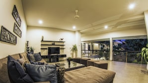 A modern living room with a sofa, coffee table, and TV, leading to a balcony with plants. - Villa Lamunan (Legian)