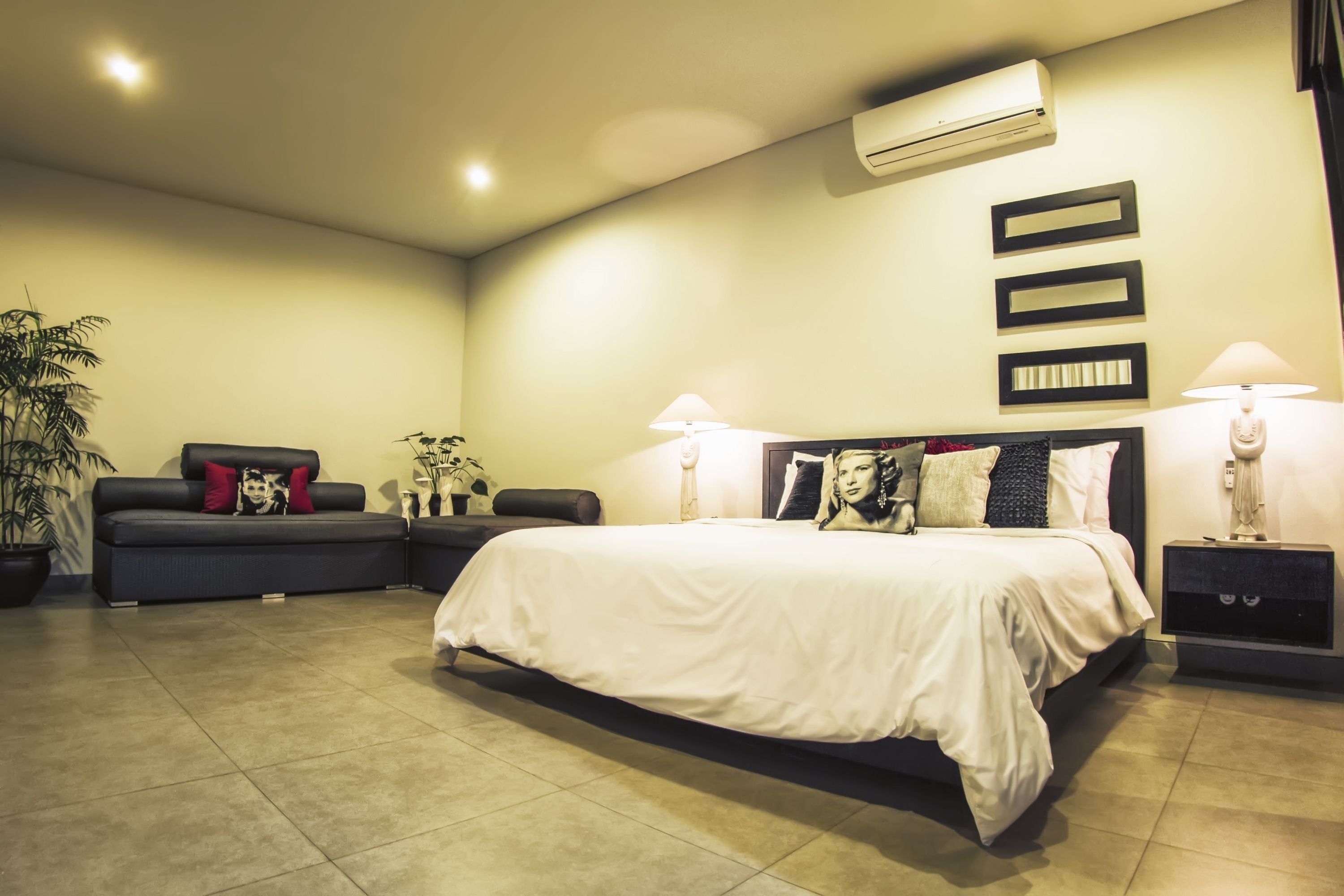 Un dormitorio moderno con una cama grande, mesitas de noche, un sofá y una planta en maceta.