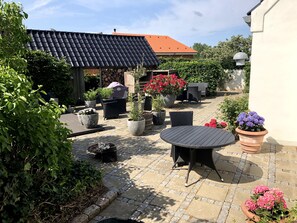 Un espace patio aménagé avec du mobilier d’extérieur, des plantes en pot et un toit recouvert de tuiles.