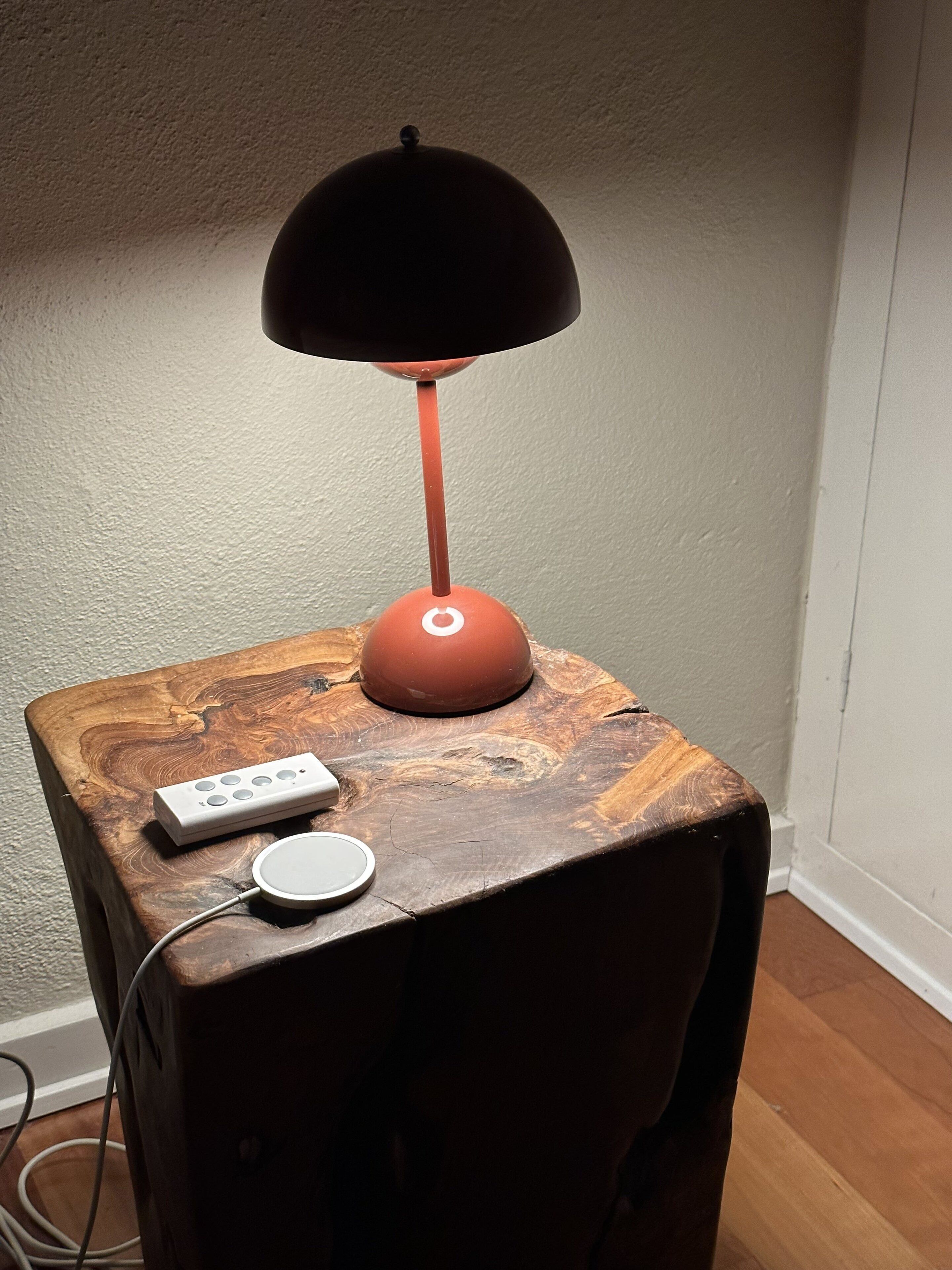 A wooden side table with a lamp, a remote control, and a power adapter.