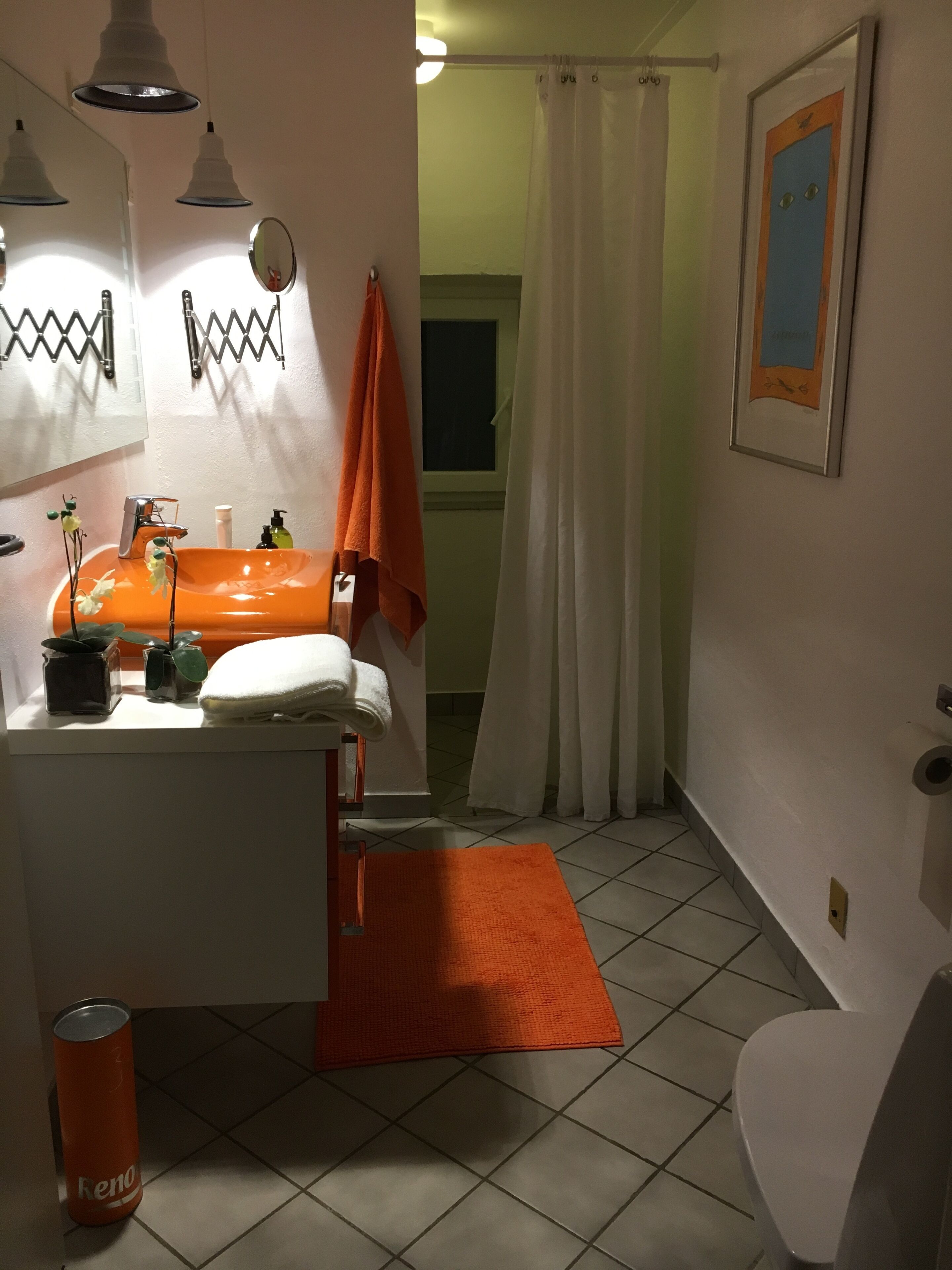 Ein Badezimmer mit einem weißen Waschbecken, einem orangefarbenen Handtuch und einem gerahmten Bild an der Wand.