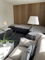 Una habitación de hotel moderna con un sofá seccional, una cama con muchas almohadas, una lámpara de pie y una planta en maceta.